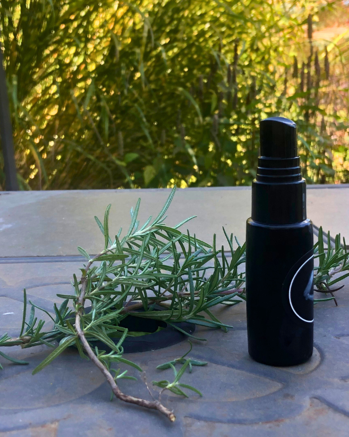 spray bottle on a table outside with sprigs of rosemary